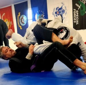 Adults practicing grappling techniques during a Brazilian Jiu Jitsu session focused on fitness and self-defense.