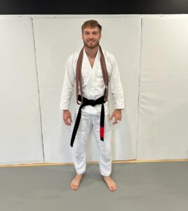 Logan Authement in a white gi, standing confidently as a Brazilian Jiu Jitsu coach at Next Generation Martial Arts.