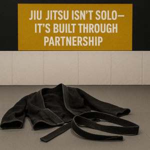 Train with different partners in BJJ symbolized by a worn black belt and gi left on gray mats beneath a yellow wall sign about partnership.